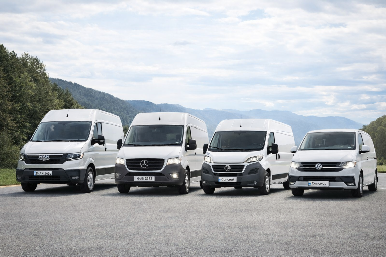 Four white delivery vans parked in a row against a mountainous backdrop.